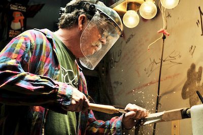 Mark Hillemann wears protective gear as he turns a table leg with his wood lathe.